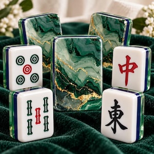 May include: A set of mahjong tiles featuring a green and white marble pattern with gold veining on the backs. The front faces display various traditional symbols in red, green, and black ink, including circles, bamboo, and Chinese characters.
