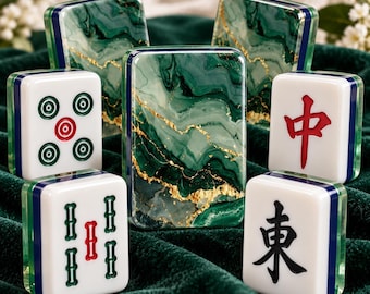 Könnte beinhalten: Ein Set aus Mahjong-Spielsteinen mit einem grün-weißen Marmormuster und goldenen Adern auf der Rückseite. Die Vorderseiten zeigen verschiedene traditionelle Symbole in roter, grüner und schwarzer Tinte, darunter Kreise, Bambus und chinesische Schriftzeichen.