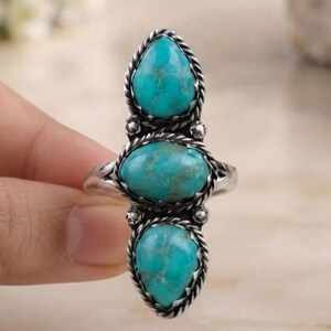 May include: A silver ring featuring three vertically aligned turquoise stones with brown veining. The stones are set in a twisted rope-style metal frame, with the top and bottom stones being teardrop-shaped and the center stone being oval-shaped.