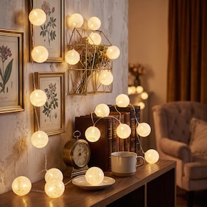 May include: A string of spherical LED lights with a textured, off-white finish. The glowing globes are connected by a thin, flexible wire, creating a warm illumination. The lights are arranged in a cascading pattern across a wall and a wooden surface.