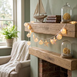 May include: A string of decorative fairy lights featuring various seashell and starfish shapes. The lights emit a warm glow and are draped across a wooden mantelpiece, highlighting the detailed textures of the individual shell and starfish forms.
