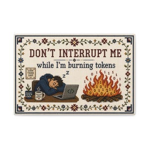 May include: A rectangular cross-stitch sampler featuring a floral border and the text "DON'T INTERRUPT ME while I'm burning tokens". It depicts a person sleeping at a desk with a laptop, a mug labeled "CAFFEINE FUELS CONTEXT", and a campfire with binary digits.