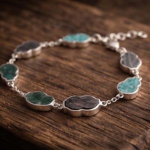 Könnte beinhalten: Ein silbernes Kettenarmband mit mehreren wolkenförmigen Fassungen, die jeweils einen polierten Edelstein in verschiedenen Schattierungen von Türkis, Dunkelgrün und Anthrazit enthalten. Das Armband besteht aus einer feinen Gliederkette und einem Verschluss.