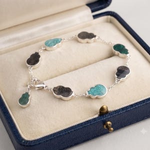 Könnte beinhalten: Ein silbernes Kettenarmband mit mehreren kürbisförmigen Edelsteinanhängern in den Farben Türkis, Dunkelgrau und Grün. Das Armband verfügt über einen Karabinerverschluss und einen hängenden Anhänger, die alle in einem feinen Gliederkettendesign angeordnet sind.