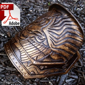 May include: A gold and brown leather armor piece with a detailed design. The armor piece has a raised design of a face with a crown and a wing. The armor piece is made of leather and has a textured surface.