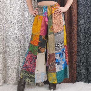Puede incluir: Pantalones de pierna ancha con un diseño de patchwork compuesto por varios paneles de tela en múltiples colores y estampados, incluyendo amarillo, azul, verde y marrón. Los pantalones tienen una cintura elástica con un pequeño detalle de borla rosa.