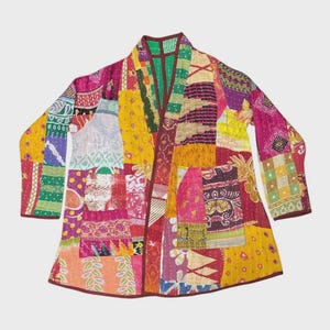 Könnte beinhalten: Eine langärmelige Jacke mit einem lebendigen Patchwork-Design aus verschiedenen bunten Stoffquadraten in Gelb-, Rosa-, Lila-, Grün- und Orangetönen. Das Kleidungsstück hat eine offene Vorderseite, einen Kragen und zwei sichtbare Vordertaschen.