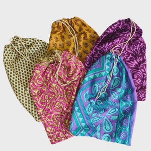 Può includere: Una collezione di cinque sacchetti con coulisse realizzati in tessuto fantasia in vari colori, tra cui giallo, viola, rosa, verde acqua e crema. Ogni sacchetto presenta una semplice chiusura con cordino bianco sulla parte superiore, con distinti motivi floreali e geometrici.