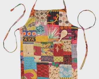 May include: A patchwork apron featuring a variety of colorful fabric squares with diverse patterns including floral, geometric, and polka dot designs. The apron includes a front pocket containing a light-colored wooden spoon with small holes.