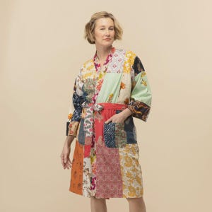 May include: A knee-length robe featuring a patchwork design with various floral and geometric patterns in shades of yellow, red, blue, green, and white. The garment includes a matching fabric tie belt at the waist and two front patch pockets.