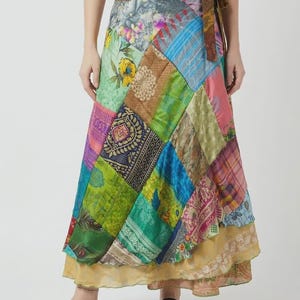 May include: A floor-length wrap skirt featuring a patchwork design of various colorful fabrics with floral, paisley, and geometric patterns. The skirt has a brown tie-waist closure and a layered hemline with a sheer, light gold-toned fabric base.