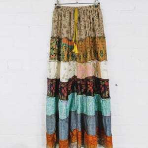 Könnte beinhalten: Ein bodenlanger Stufenrock aus einem Patchwork verschiedener Stoffe mit Blumen-, Paisley- und Streifenmustern. Der Rock verfügt über einen elastischen Bund mit einem leuchtend gelben Kordelzug und eine geraffte, fließende Silhouette.