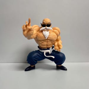 May include: A muscular bald figurine with a white beard and mustache, wearing black sunglasses, dark blue pants with a white waistband, and black shoes. The figure is in a dynamic pose with one hand extended forward and the other hand clenched.