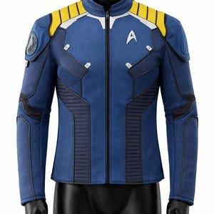 Puede incluir: Una chaqueta azul de manga larga con cuello alto, cremallera central y paneles amarillos en los hombros. La prenda incluye una insignia delta de Starfleet blanca en el pecho, un parche circular en el hombro derecho y paneles texturizados.