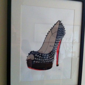 Puede incluir: Obra de arte enmarcada con una ilustraci&oacute;n de un zapato de tac&oacute;n alto. El zapato es negro con tachuelas plateadas, suela roja y tac&oacute;n rojo. La palabra "Par&iacute;s" est&aacute; impresa en el lateral. La obra est&aacute; en un marco negro.