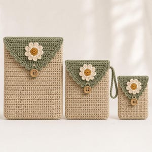 Puede incluir: Tres estuches rectangulares de ganchillo de diferentes tamaños, cada uno con cuerpo beige, solapa triangular verde salvia con borde festoneado, aplicación de margarita blanca y amarilla y un botón de madera marrón.
