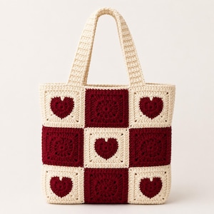 Pode incluir: Uma bolsa de crochê com um padrão xadrez de quadrados creme e vermelho escuro. O design alterna entre quadrados vermelho escuro sólidos e quadrados creme contendo um motivo de coração vermelho escuro. A bolsa tem duas alças creme.