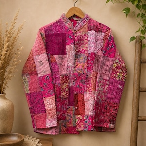 Könnte beinhalten: Eine langärmelige Steppjacke mit Patchwork-Design in verschiedenen Rosa-, Magenta- und Rottönen. Die Jacke hat einen Stehkragen, eine Knopfleiste auf der Vorderseite und sichtbare Steppnähte, die sich über das gesamte Stoffmuster ziehen.