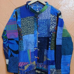 May include: A long-sleeve quilted jacket featuring a patchwork design of various blue, green, and purple fabric patterns. The jacket has a mandarin collar, a front button closure, and two front pockets, all constructed from stitched fabric panels.