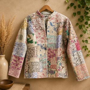 May include: A long-sleeve quilted jacket featuring a patchwork design composed of various floral and geometric fabric patterns in shades of pink, blue, yellow, and green. The jacket has a mandarin collar, a front button closure, and two pockets.
