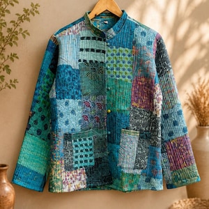 May include: A long-sleeve quilted jacket featuring a patchwork design in various shades of blue, teal, and green. The jacket has a mandarin collar, a front button closure with multicolored buttons, and two square patch pockets on the front.