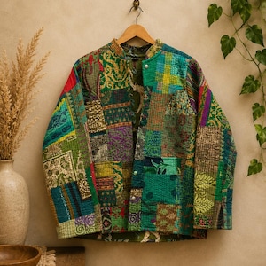 Peut inclure: Une veste matelassée à manches longues présentant un motif patchwork avec divers tissus aux tons verts, jaunes et rouges. La veste possède un col officier, une fermeture boutonnée à l'avant avec des boutons-pression argentés et deux poches.