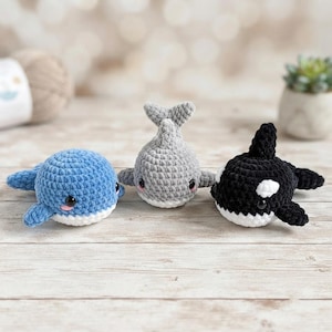 Peut inclure: Trois petits jouets en peluche crochetés en fil doux, représentant une baleine bleue, une baleine grise et une orque noire et blanche. Chaque créature a des yeux noirs ronds, de petites joues roses et un dessous blanc, avec un maillage texturé.