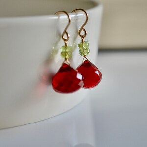 May include: Red and green gemstone dangle earrings with gold-tone hooks. The red gemstones are faceted and teardrop shaped. The green gemstones are small and round.