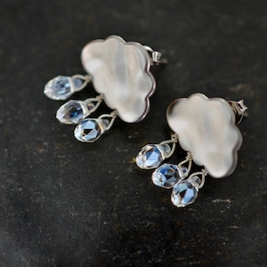 May include: Silver cloud earrings with dangling crystal raindrops. The earrings are a whimsical and delicate design.