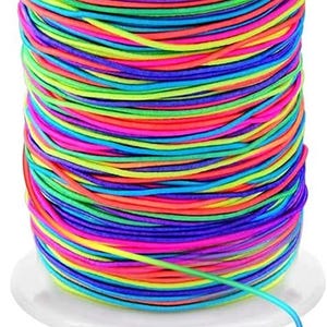 May include: A spool of multi-colored elastic cord featuring vibrant neon shades of pink, blue, green, yellow, and orange wrapped tightly around a white plastic cylinder. A single strand of the thin, flexible cord extends from the base of the spool.