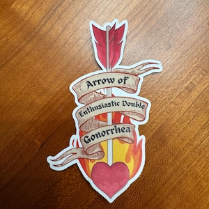 May include: A sticker featuring a red arrow piercing a pink heart, surrounded by orange and yellow flames. A beige banner wraps around the arrow with the black text 'Arrow of Enthusiastic Double Gonorrhea' written in a decorative serif font.