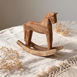 Könnte beinhalten: Eine hellbraune Schaukelpferd-Figur aus Holz mit geschnitzter Mähne, ausgeprägter Schnauze und glatter Oberfläche. Das Pferd ist auf zwei geschwungenen Kufen montiert, die eine sanfte Schaukelbewegung ermöglichen und die Holzmaserung zeigen.