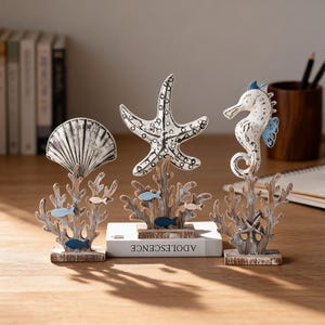 May include: Three decorative tabletop ornaments featuring a white seashell, a white starfish, and a white seahorse, each mounted on a brown textured coral-shaped base with small blue and tan fish accents, standing on rectangular wooden bases.