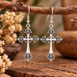 May include: A pair of silver-toned dangle earrings featuring an ornate cross design with intricate filigree detailing at each point and a central circular element. The earrings are suspended from simple silver-toned metal hooks for pierced ears.