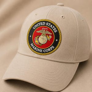 Może przedstawiać: Beżowa czapka z daszkiem z okrągłą, haftowaną naszywką z przodu. Naszywka przedstawia emblemat United States Marine Corps ze złotym orłem, globusem i kotwicą na czerwonym tle, otoczony złotą obwódką przypominającą linę z czarnym napisem.