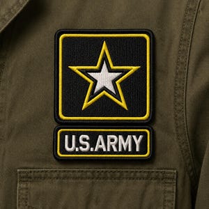 May include: An olive green jacket featuring two embroidered patches on the chest. The top square patch displays a white star with a yellow border on a black background. The rectangular patch below features the white text U.S.ARMY with a yellow border.
