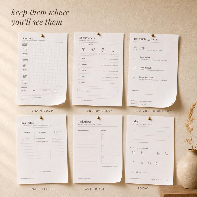 Six printed planner sheets pinned to a warm plaster wall with brass pins: brain dump, today, energy check, too much right now, task triage and small refills. Overlay text reads keep them where you will see them.