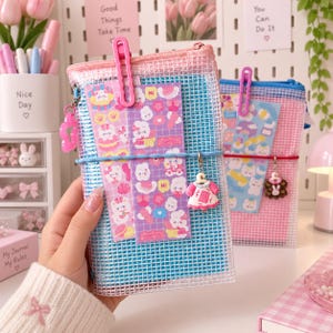 Puede incluir: Un estuche rectangular de malla transparente con cremallera rosa e interior azul. Incluye un clip de plástico rosa, una banda elástica azul y un pequeño dije con forma de vestido. Tiene adheridas dos hojas verticales de pegatinas con personajes.