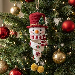 May include: A crocheted snowman ornament featuring a red top hat with a small green tree, a white face with an orange nose, and a red and white striped scarf. The body is a white spiral decorated with red and green beads and two gold pom-poms.