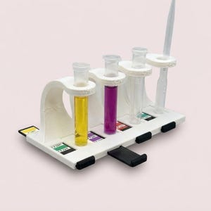 以下が含まれることがあります： 4本の透明なガラス管を保持する白いプラスチック製の試験管立て。1本には黄色い液体、もう1本には紫色の液体が入っており、2本は空です。透明なプラスチック製のスポイトが差し込まれています。色分けされたテストストリップが見えます。