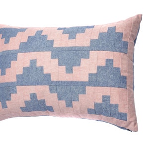 May include: A rectangular pillow with a geometric pattern in shades of pink and blue. The pillow is made of a soft, textured fabric.