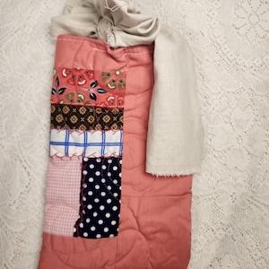 May include: A rectangular quilted pouch featuring a patchwork design of various fabric patterns including floral, geometric, and polka dot prints in shades of pink, blue, black, and white, with a solid pink back and a beige fabric tie closure.