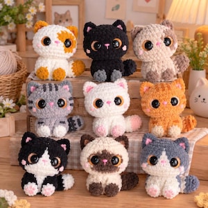 May include: A collection of nine small, crocheted plush cats arranged in three rows. Each cat features a soft, textured yarn body, large glossy black eyes, a small pink nose, and a rounded tail. The cats vary in colour, including white with orange patches, solid black, light brown, grey tabby, solid white, orange tabby, black and white, Siamese-style, and grey and white.