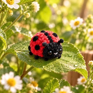 May include: A small, round, crocheted ladybug figurine featuring a bright red back with black spots and a black head with two antennae. The ladybug has two shiny black eyes and a tiny white stitched mouth, resting on a green leaf with water droplets.
