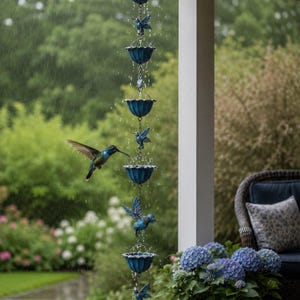 May include: A blue metal rain chain featuring a series of alternating scalloped cups and hummingbird figures. Water cascades down the vertical chain, which is suspended from a roof eave, while a hummingbird flies near the structure in the rain.