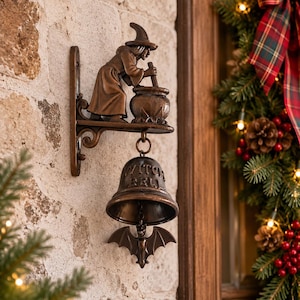 May include: A bronze-toned metal wall-mounted bell featuring a figure of a witch stirring a cauldron on the top bracket. The bell is inscribed with the text WITCH BELL and has a bat-shaped clapper hanging from the center of the bell interior.