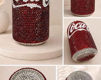 May include: A cylindrical beverage can covered in deep red rhinestones with a white rhinestone Coca-Cola logo. The top and bottom rims are lined with silver rhinestones, and the top pull tab is also encrusted with matching silver rhinestones.