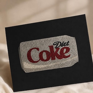 May include: A rectangular black box featuring a central graphic of a Diet Coke can rendered in sparkling rhinestones. The design uses clear crystals for the background, red crystals for the word Coke, and black crystals for the word Diet.