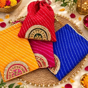 May include: A collection of four drawstring pouches in red, yellow, magenta, and blue, each featuring diagonal silver stripes and a semi-circular decorative patch with gold-toned embroidery, mirrors, and sequins on the front lower section.