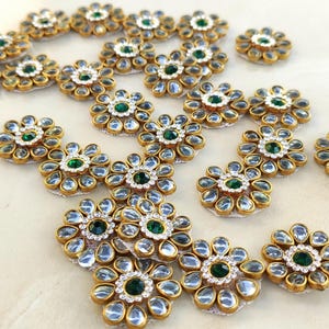 Peut inclure: Une collection d'ornements en forme de fleur avec une pierre centrale circulaire vert foncé entourée d'un anneau de petits cristaux clairs et d'une couche extérieure de pierres claires en forme de goutte serties dans des cadres en métal doré.